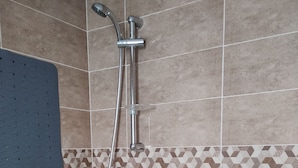 A shower with a handheld showerhead and a wall-mounted faucet, tiled walls with a geometric pattern, and a blue mat on the floor. - Hammam lif Apartment Magnificent Mountain View (Hammam-Lif)