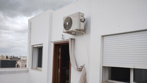 A room with a white exterior, a wooden door, a window with blinds, and an air conditioning unit mounted on the wall. - Hammam lif Apartment Magnificent Mountain View (Hammam-Lif)