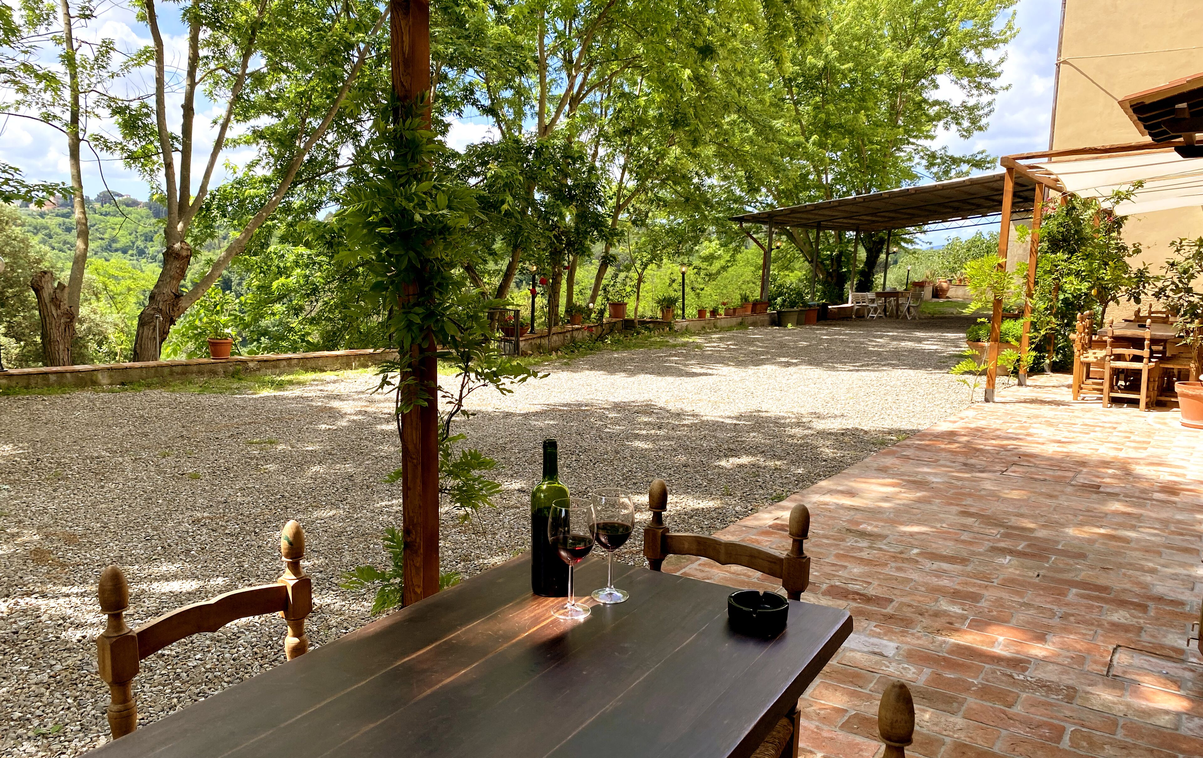 Un patio con una mesa lista para dos personas, rodeado de grava y árboles.