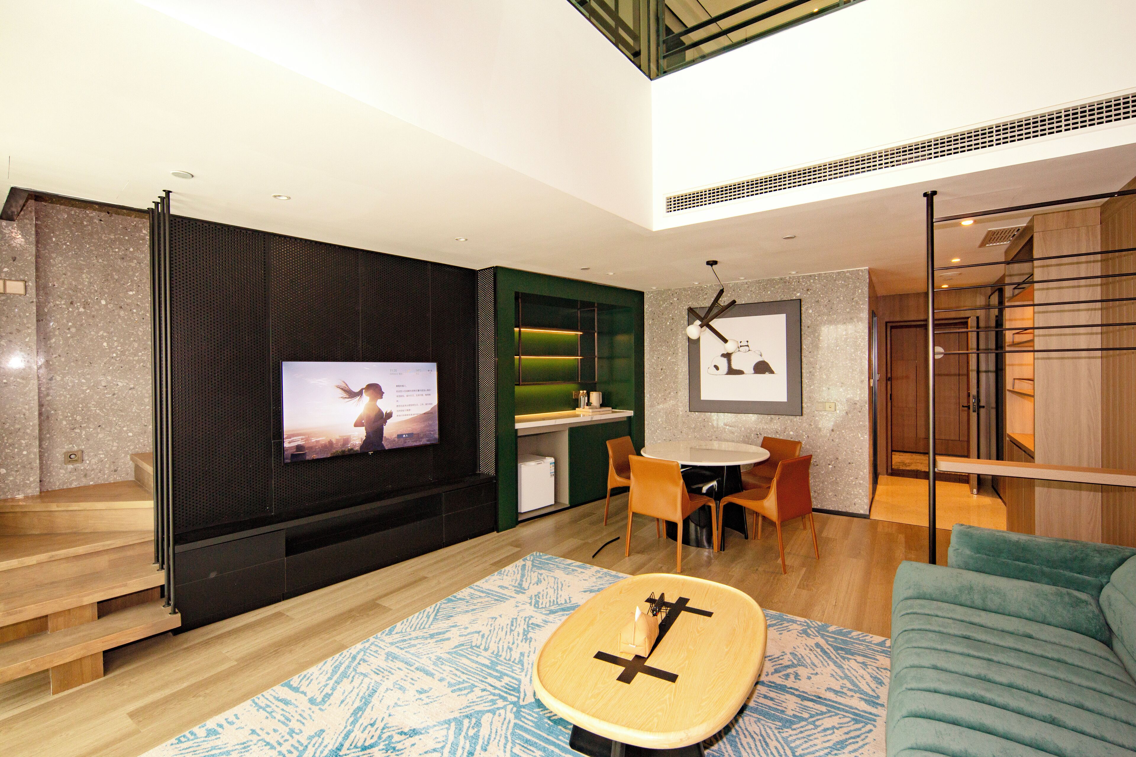 Una sala de estar moderna con un televisor de pantalla plana, un comedor y una escalera que lleva a un nivel superior.