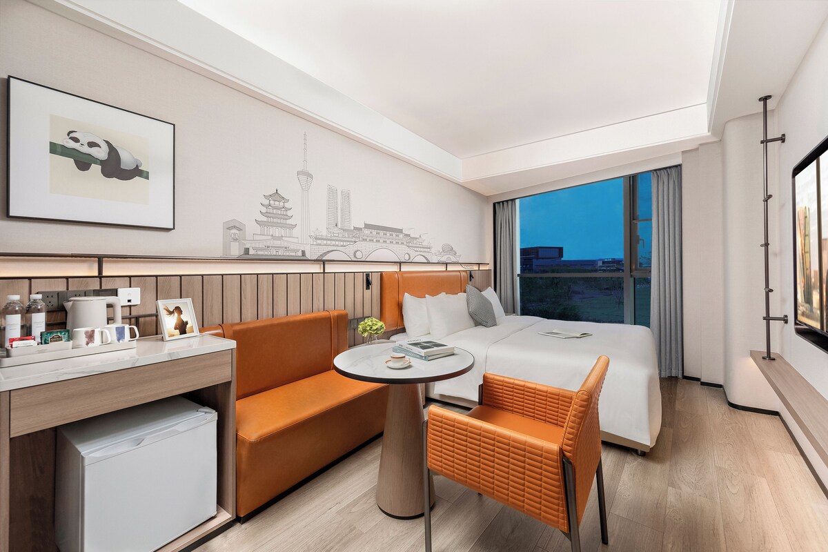 A modern hotel room with a bed, orange furniture, a small table, and a cityscape mural on the wall.