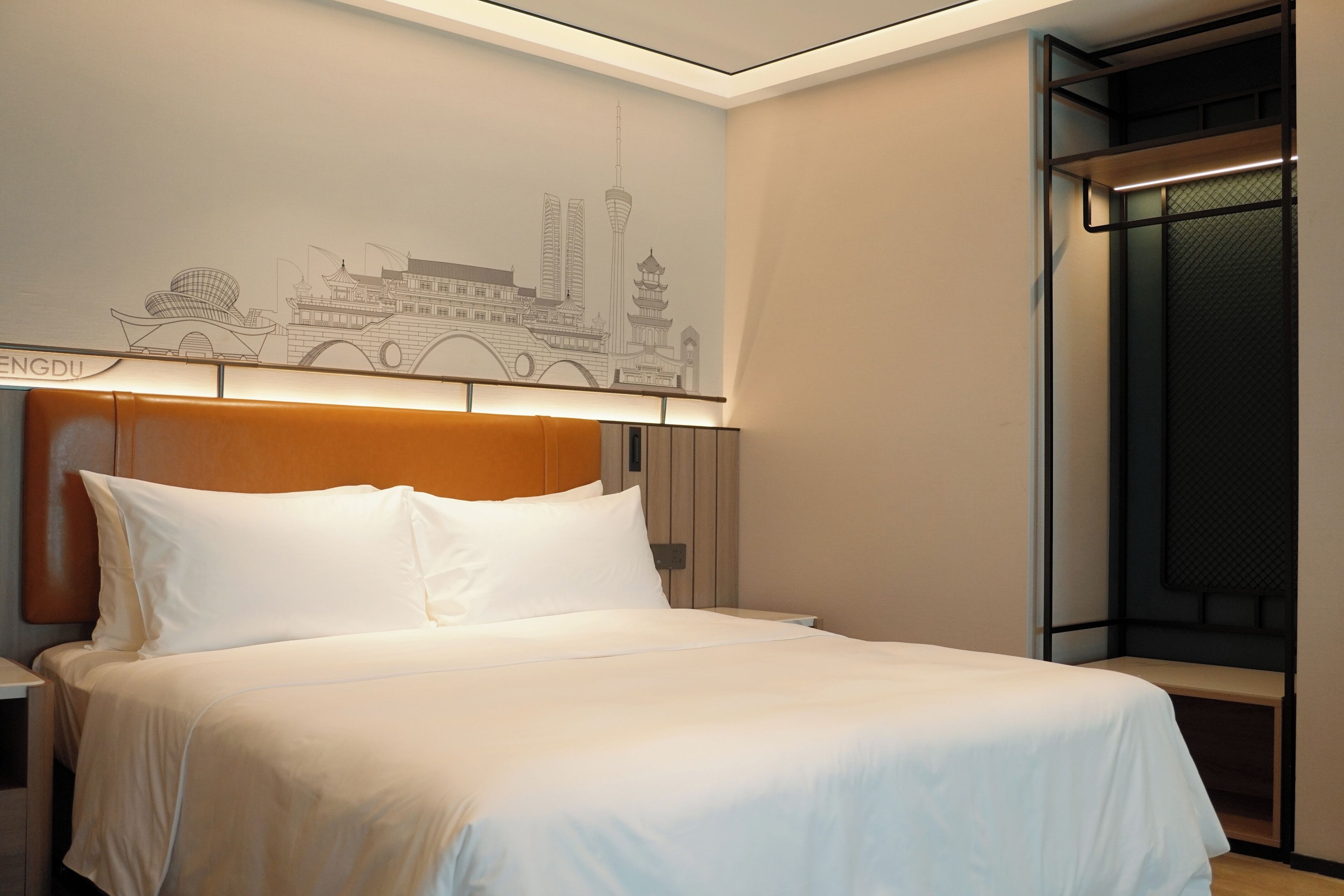 A modern hotel room with a large bed, a headboard with integrated lighting, a wall mural of a cityscape, and a window with a view of the city.
