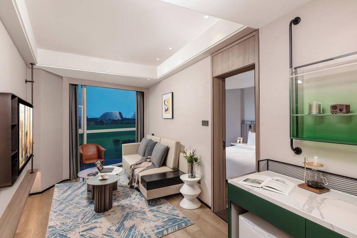 Ett modernt hotellrum med ett stort fönster, en soffa, ett soffbord, ett litet sidobord och en spegel med en grön ram.