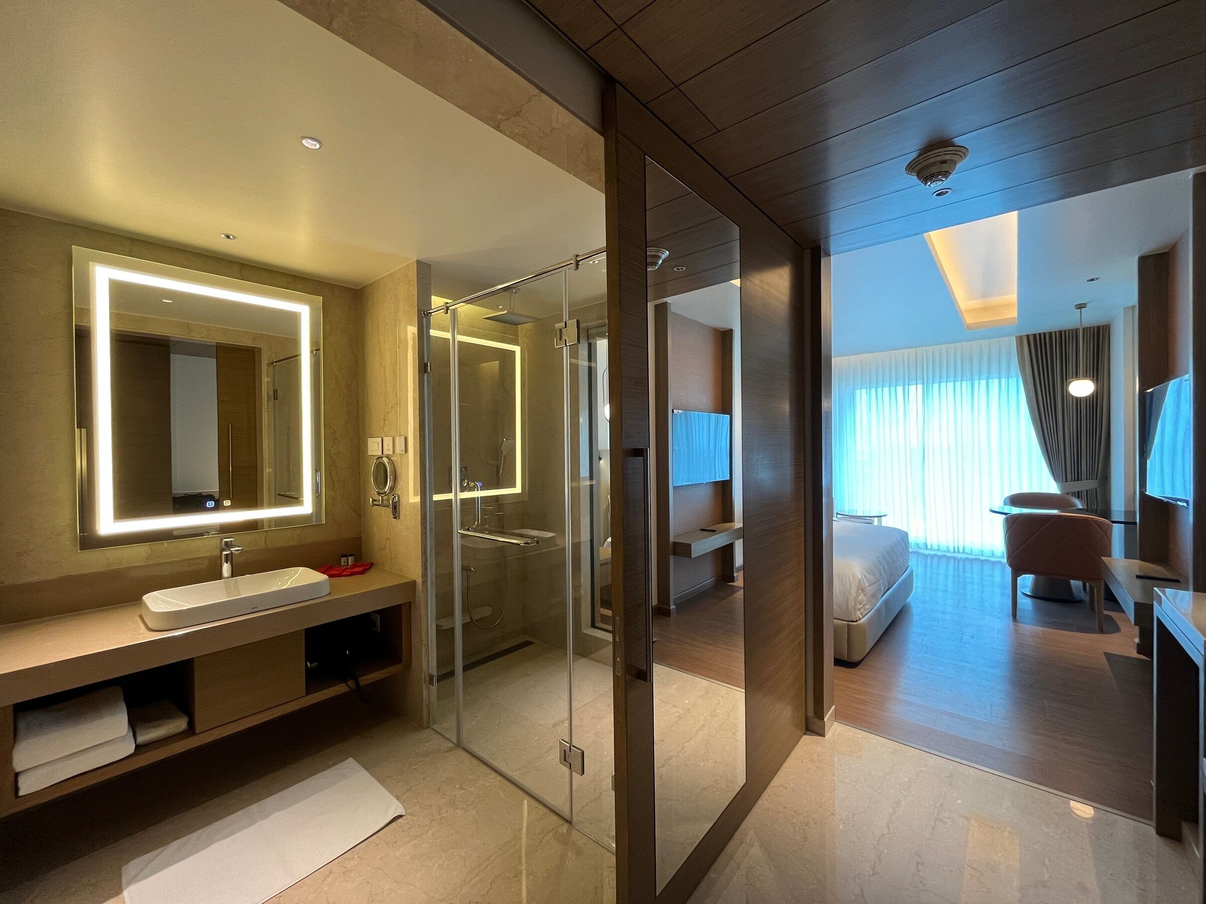 Un baño moderno con ducha envuelta en vidrio, un espejo grande con iluminación debajo del mueble y un lavamanos con toallero.