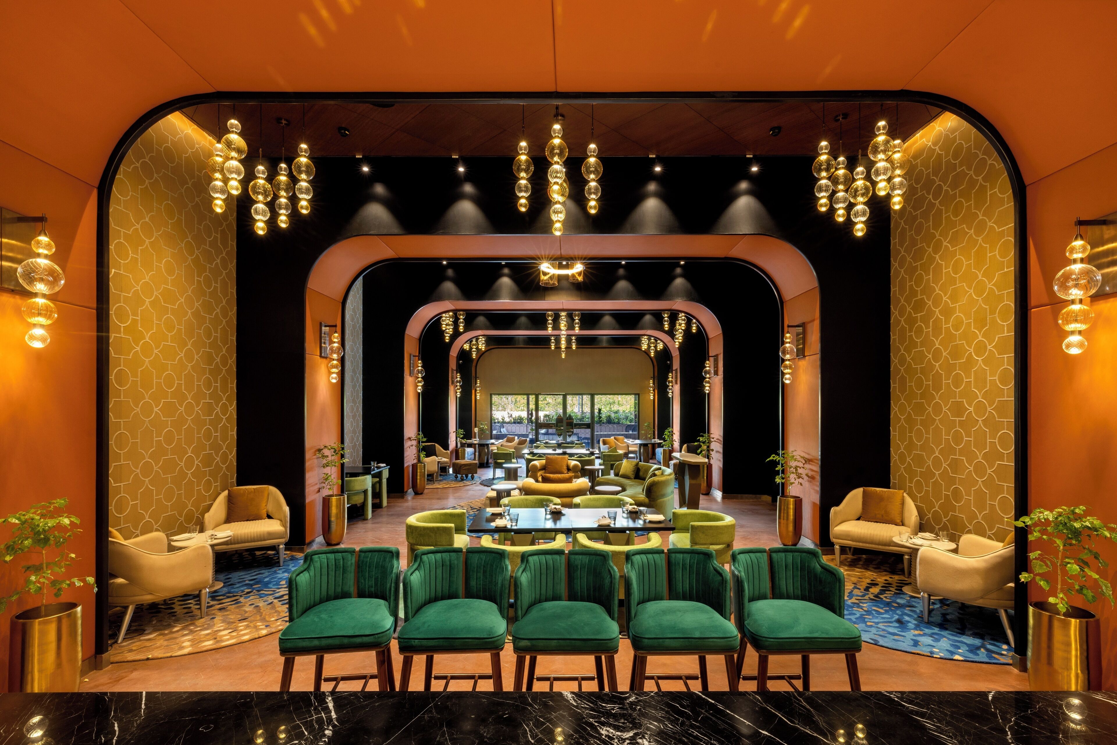 A modern hotel lobby with a central seating area, multiple chandeliers, and a geometric patterned wall.