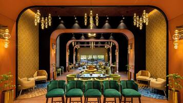 A modern hotel lobby with a central seating area, multiple chandeliers, and a geometric patterned wall.