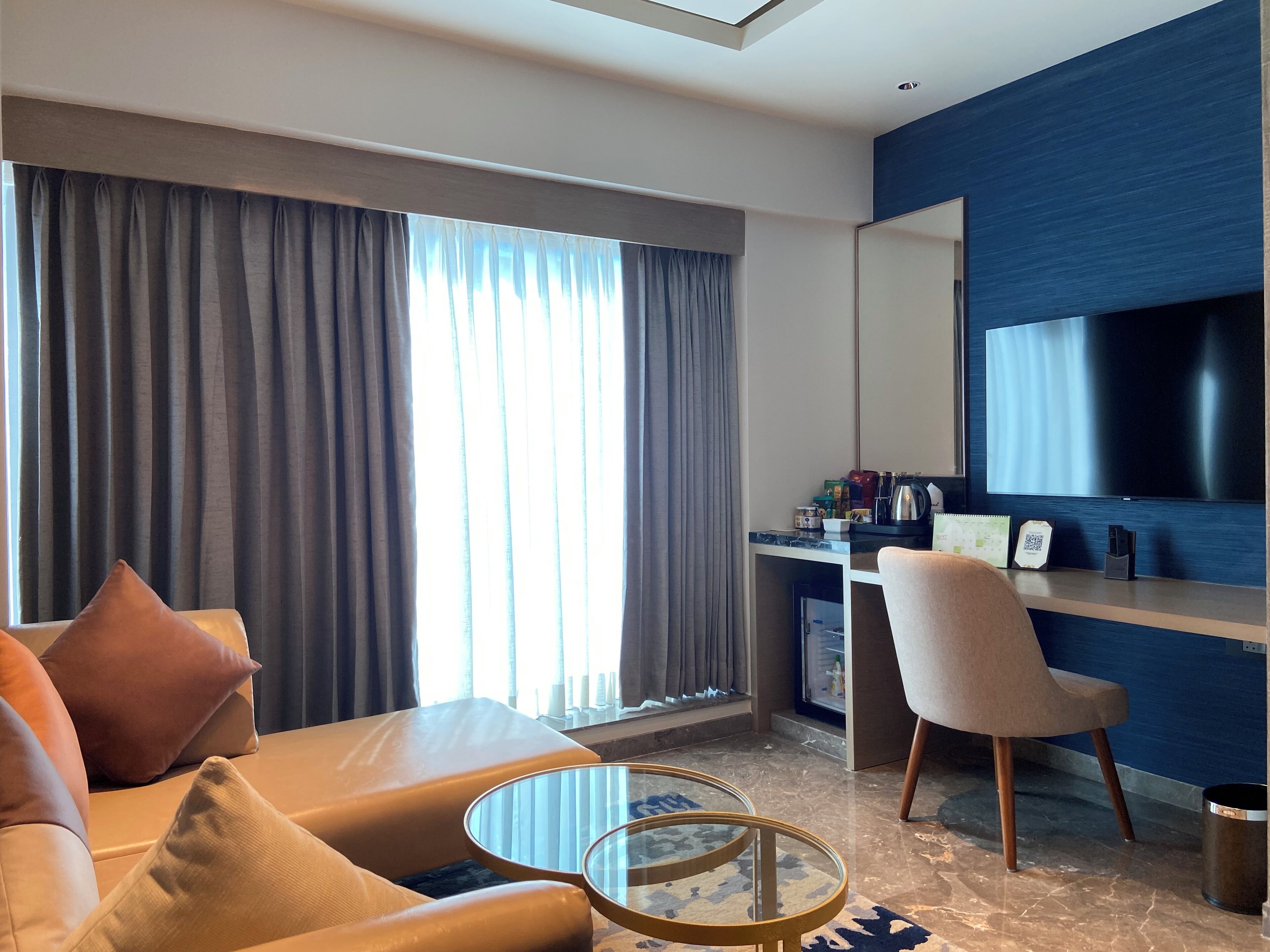 A modern hotel room with a sofa, a glass coffee table, a desk with a computer and a flat-screen TV.