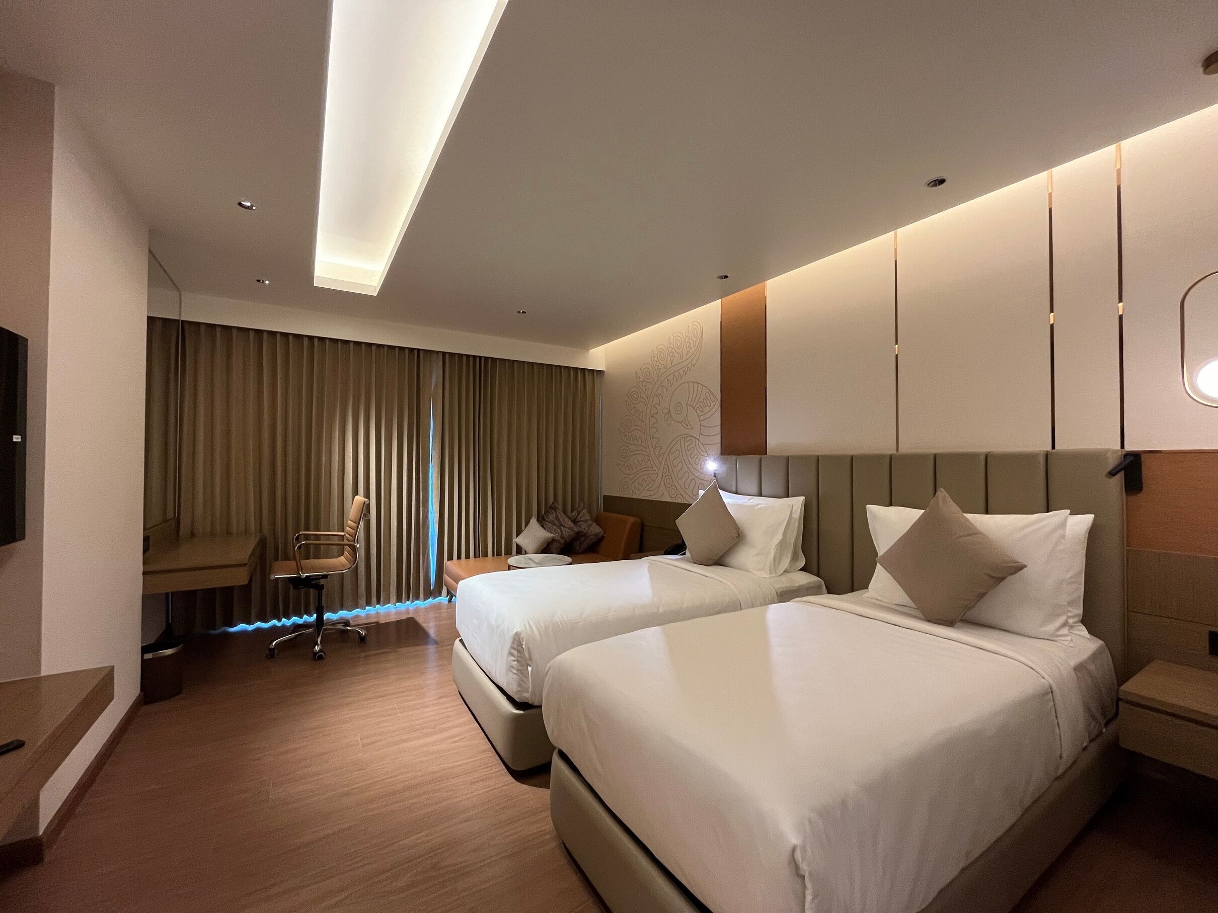 A hotel room with two beds, a desk, a chair, and a television.