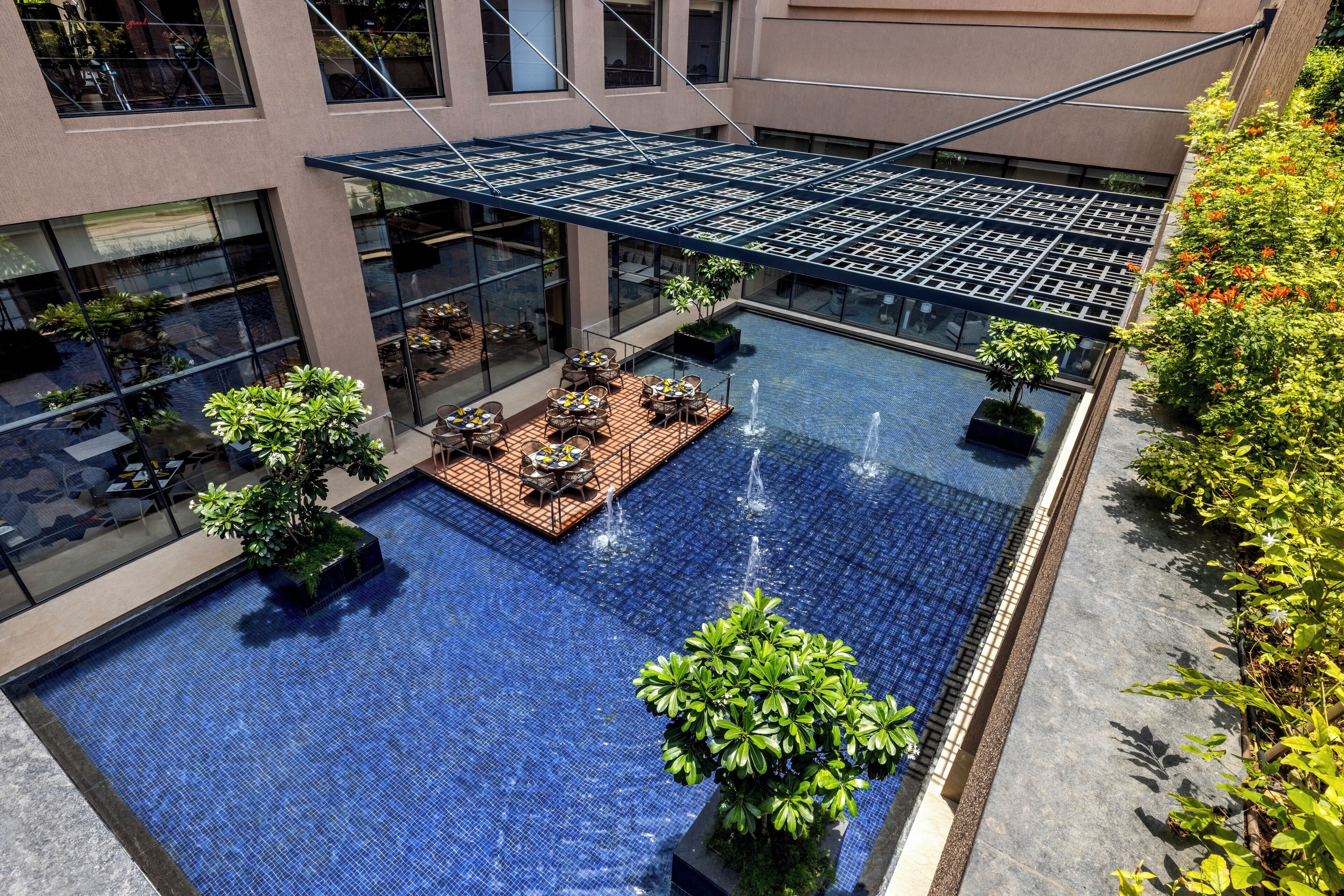 A rooftop pool with a glass balustrade, surrounded by outdoor seating and greenery.