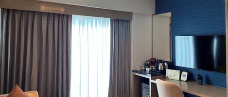 A modern hotel room with a large bed, a desk with a computer, a TV, and a minibar.