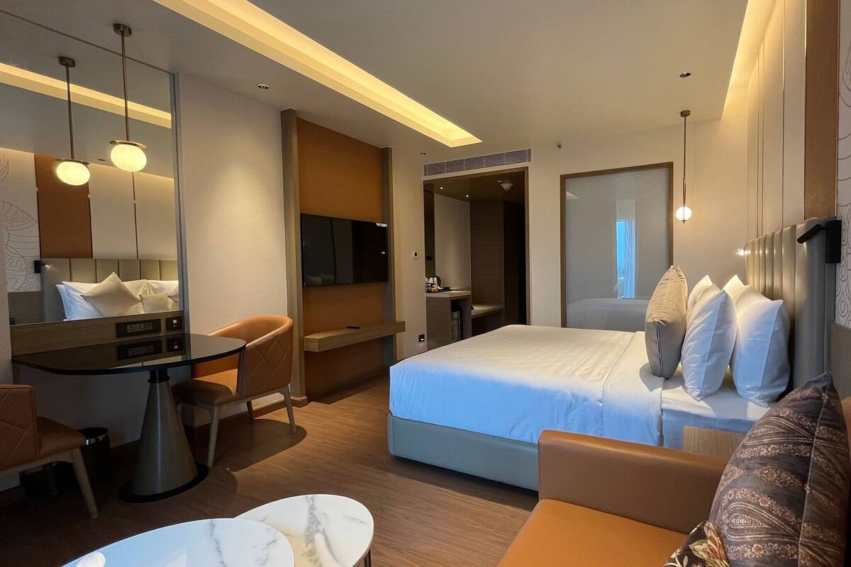 Een moderne hotelkamer met een bed, een bureau, een stoel, een bank en een grote spiegel.