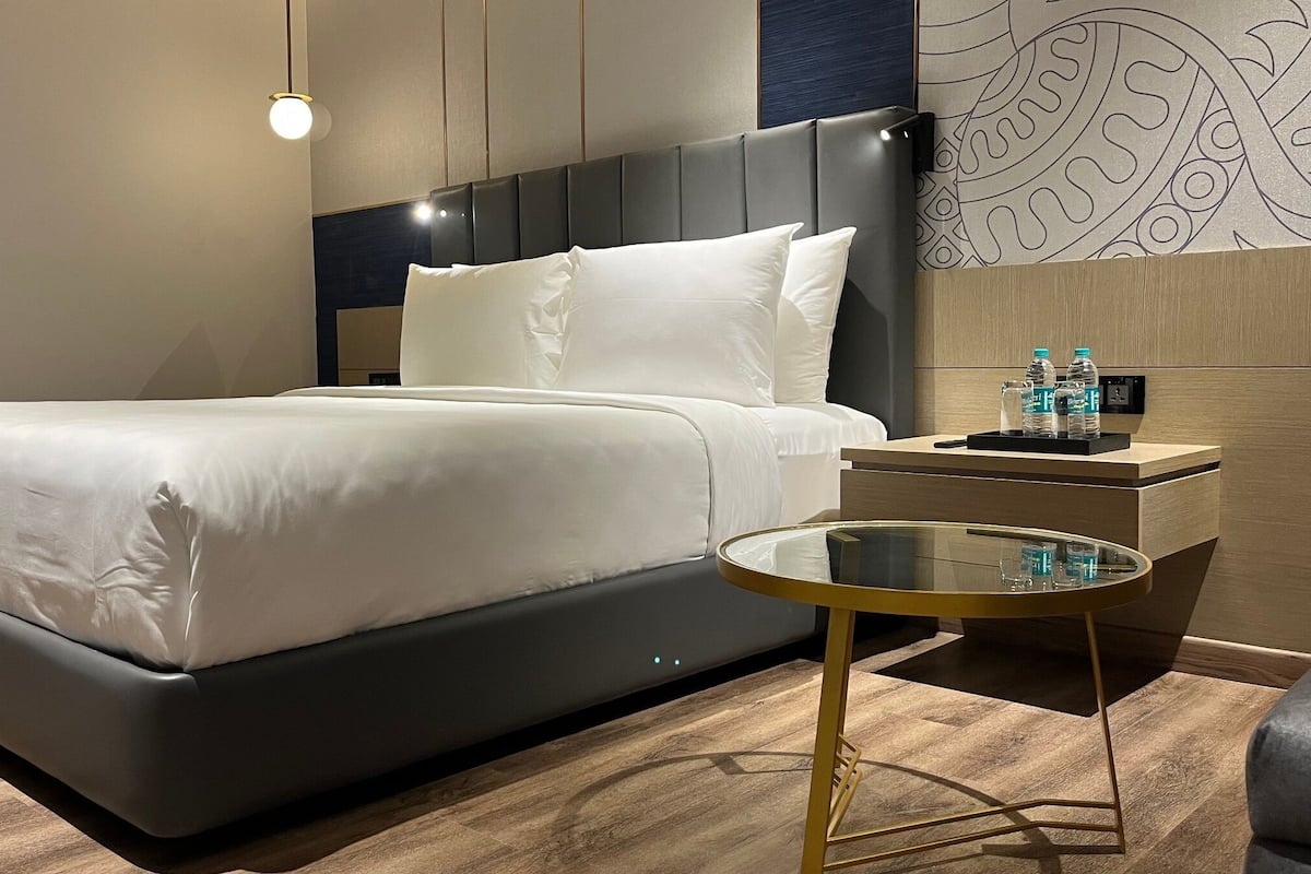 Een moderne hotelkamer met een groot bed, een nachtkastje met een glazen blad en een nachtkastje dat aan de muur is bevestigd.