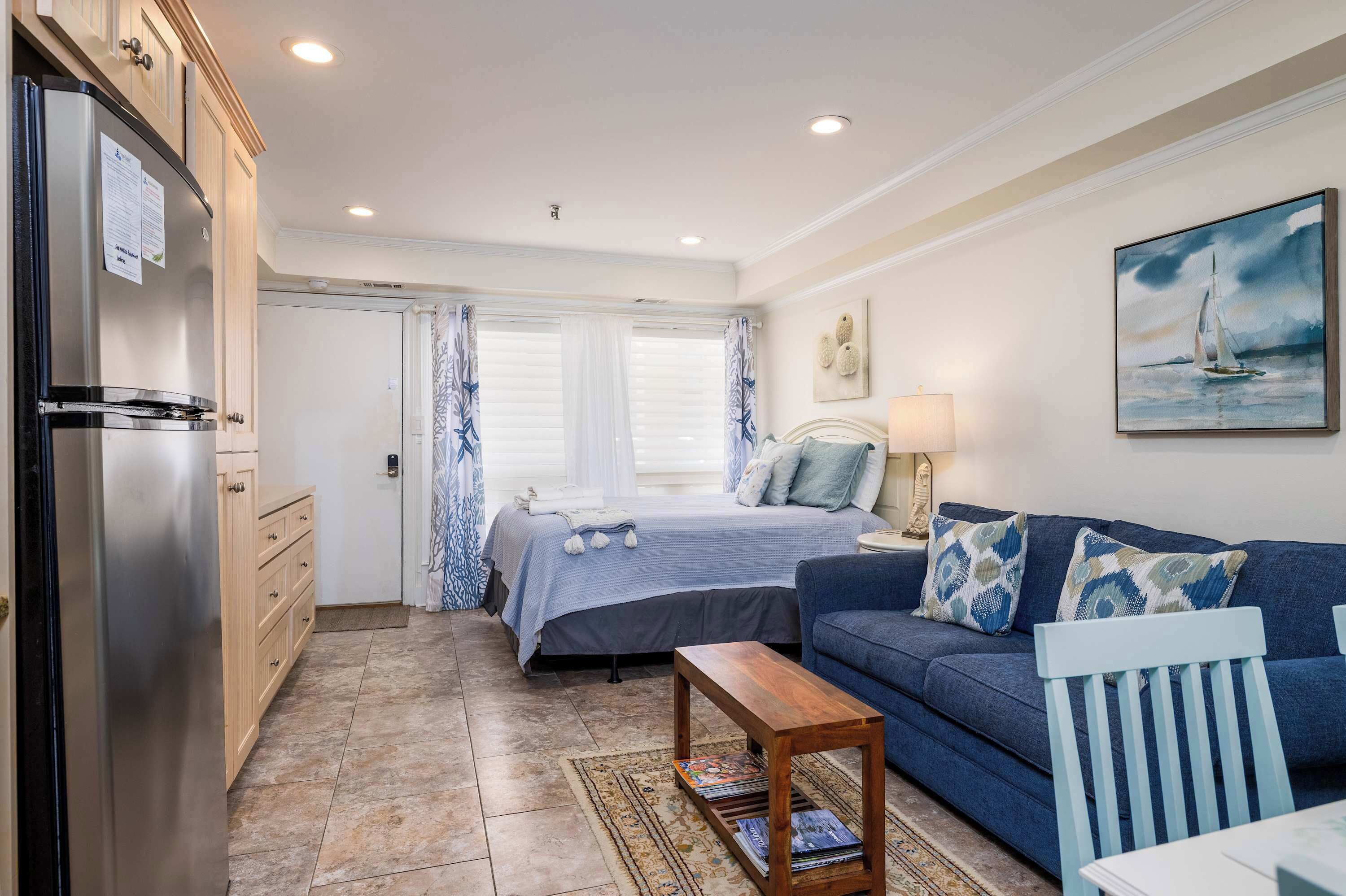 A compact room with a bed, a sofa, a wooden coffee table, and a refrigerator.
