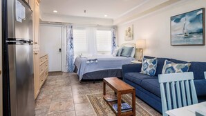 A compact room with a bed, a sofa, a wooden coffee table, and a refrigerator.