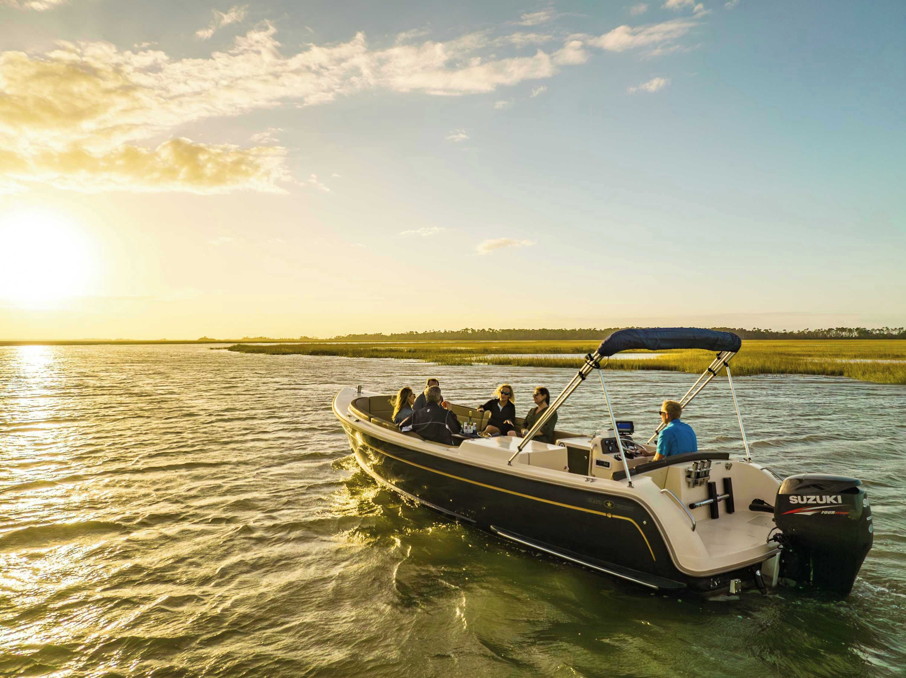 A boat with a Suzuki outboard motor, passengers, and a calm water body with a distant shoreline.