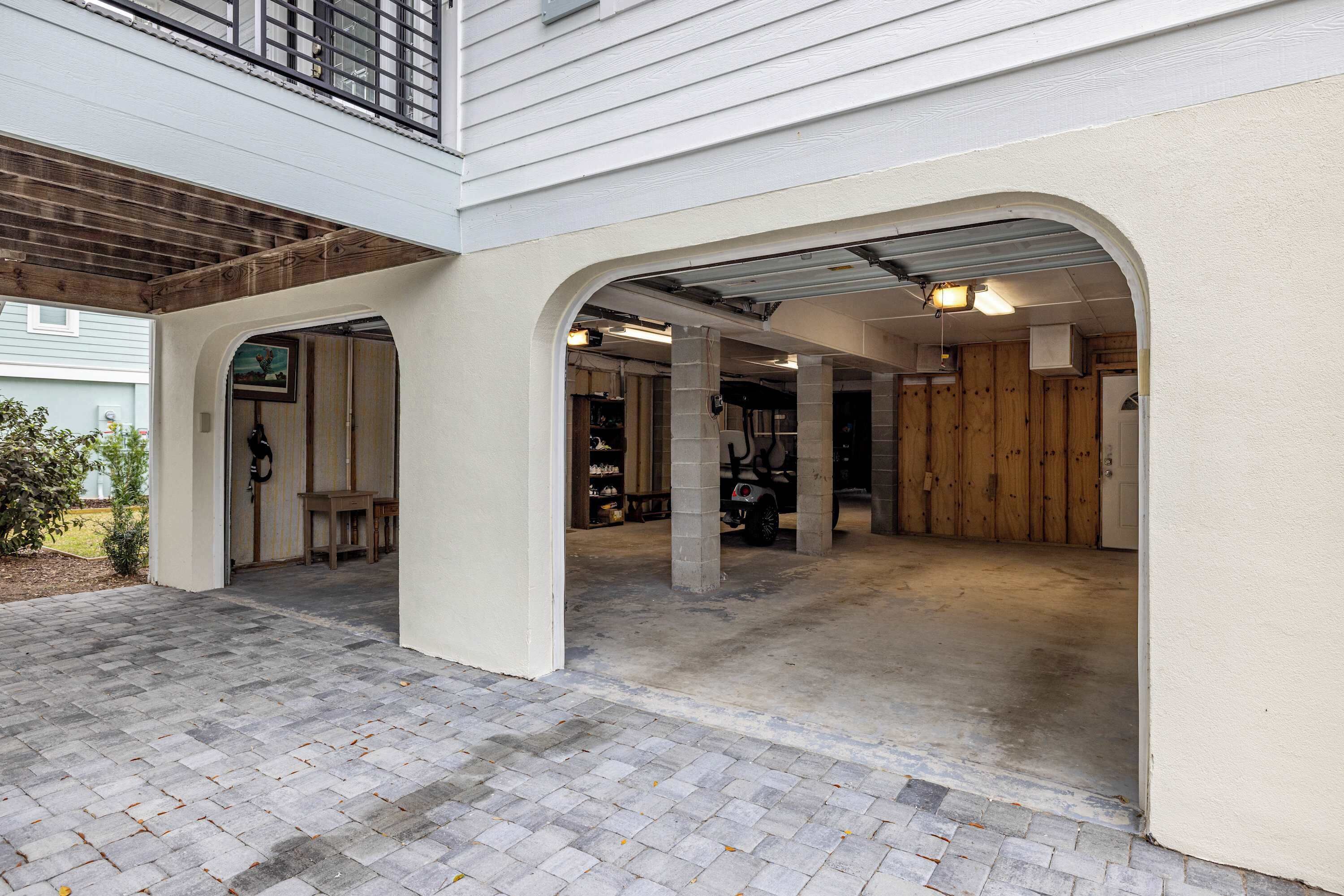 A covered garage area with a brick floor, wooden pillars, and a vehicle parked inside.