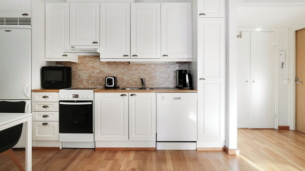A compact kitchen with white cabinets, a microwave, an oven, a dishwasher, and a coffee maker. - Kotimaailma Aparthotel Kamppi 1BR with balcony (Helsinki)