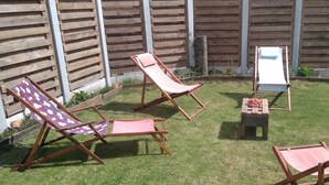 A backyard with wooden fences, two lounge chairs, and a small table with a fruit bowl.