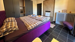 Un dormitori amb un llit gran, armaris foscos, un panell de capçaló de fusta i un radiador.