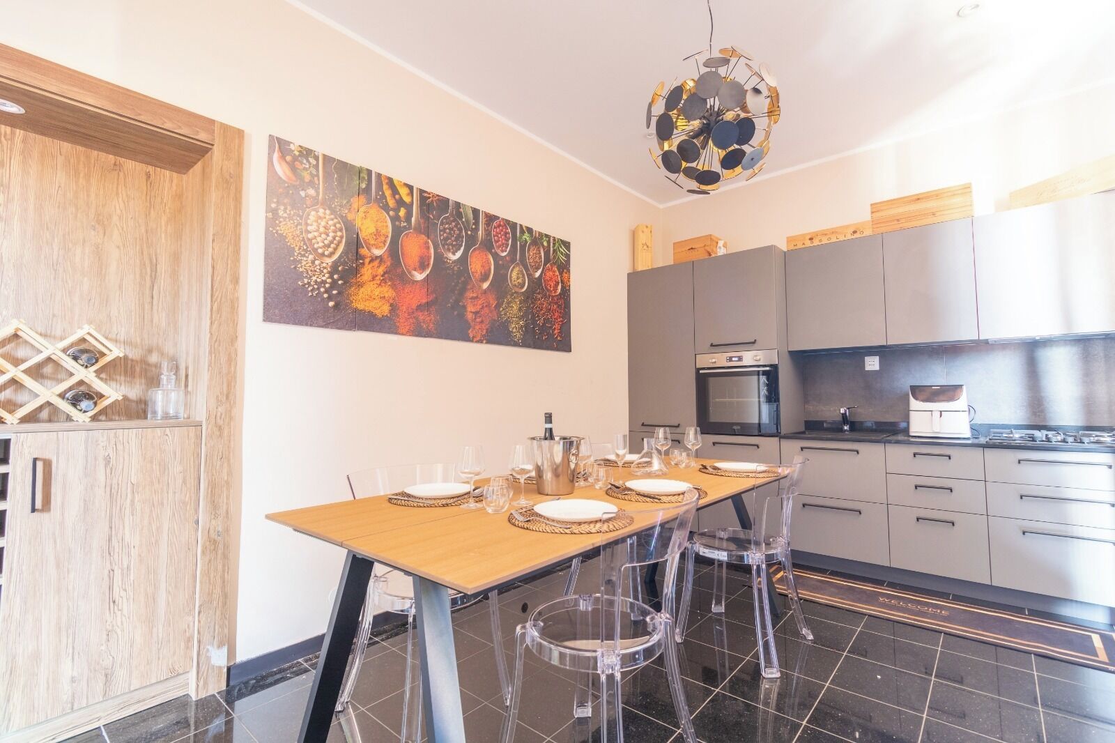 A modern kitchen with a dining area, featuring a wooden table, clear chairs, and a large abstract painting on the wall.