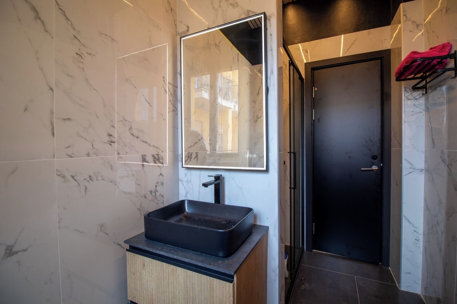 Un baño moderno con un lavamanos tipo recipiente negro, un espejo grande y una puerta negra.
