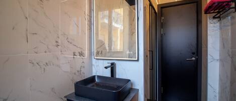 Un baño moderno con un lavamanos tipo recipiente negro, un espejo grande y una puerta negra.