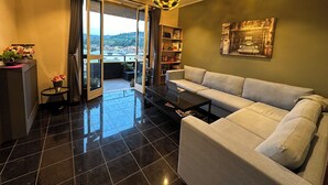 Un saló modern amb un sofà, una taula de centre i una prestatgeria. Hi ha una finestra gran amb cortines, una vista cap a l'exterior i una lluminària esfèrica singular.