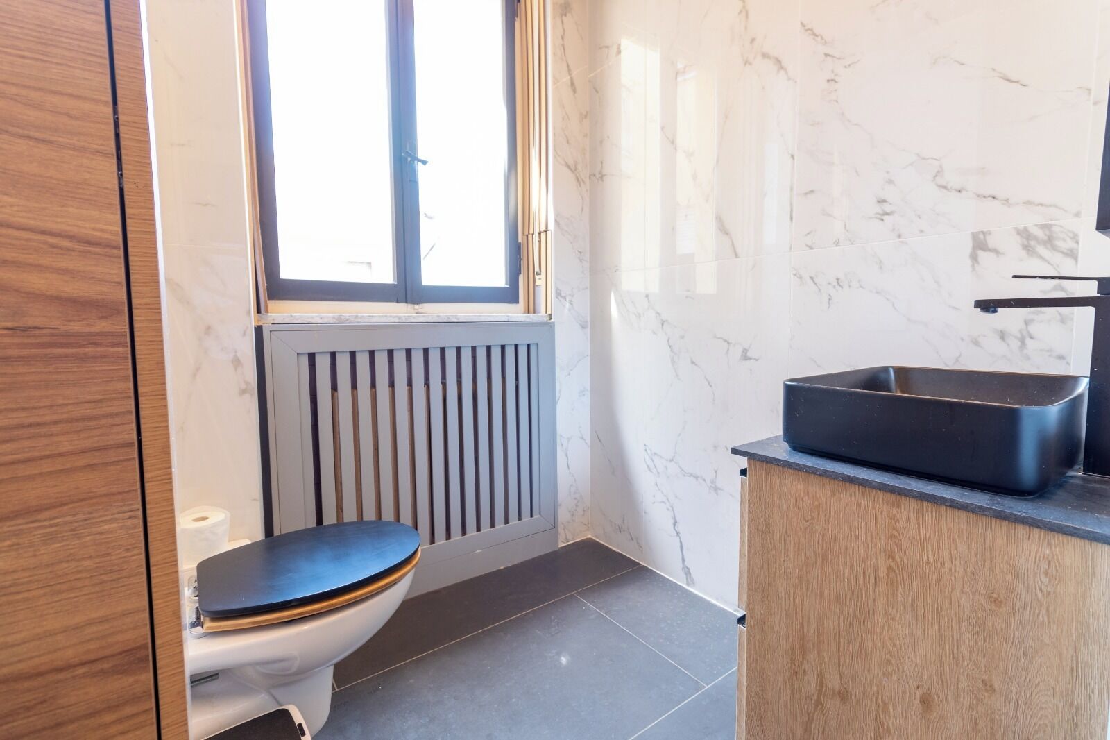 Une salle de bain moderne équipée de toilettes, d’un radiateur et d’un lavabo avec un receveur noir.