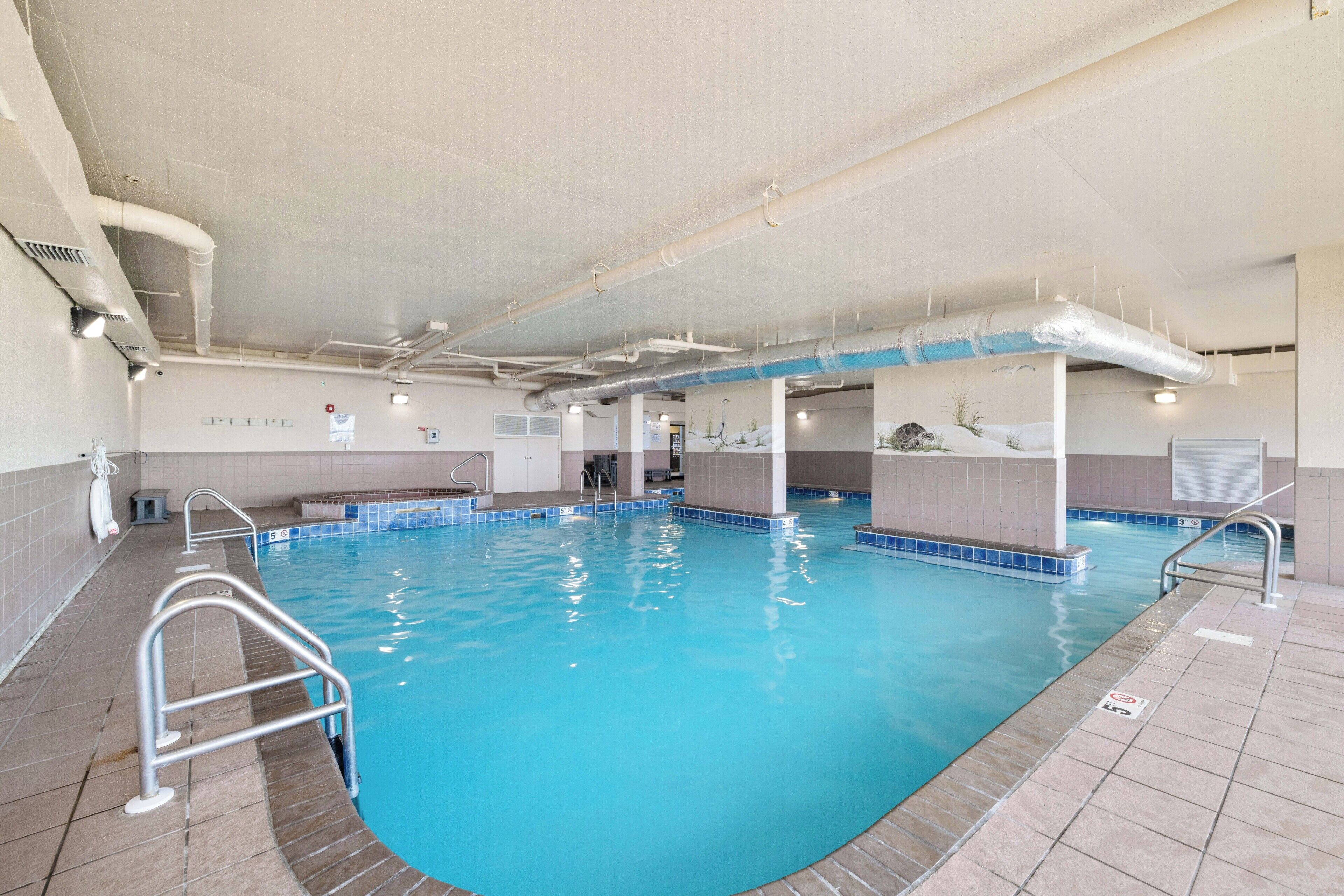 An indoor swimming pool with clear water, tiled walls, and a ceiling with visible ductwork.