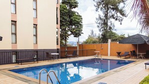 En swimmingpool med liggestole og borde, omgivet af en bygning med balkon.