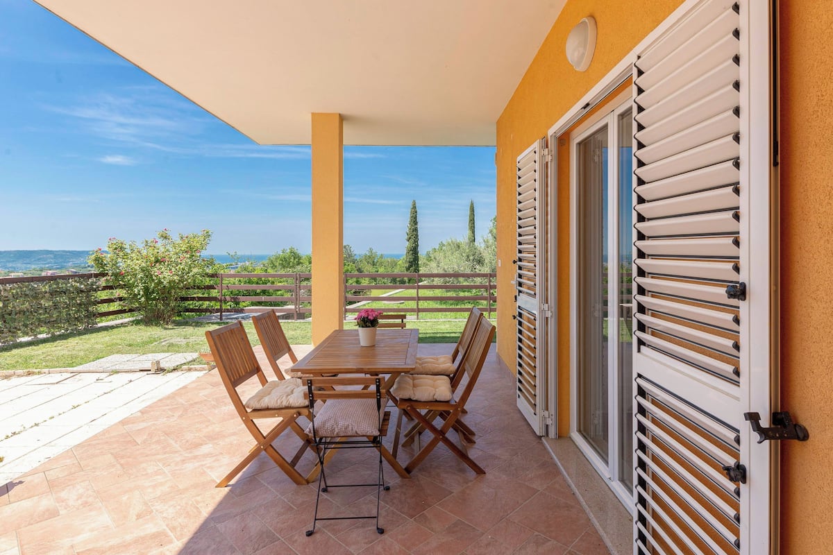 A patio with a table and chairs, a view of the countryside, and a door with shutters.