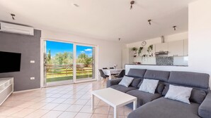 A modern living room with a grey sofa, a white coffee table, and a TV on the left. - Serene Retreat St. Anton (Koper)