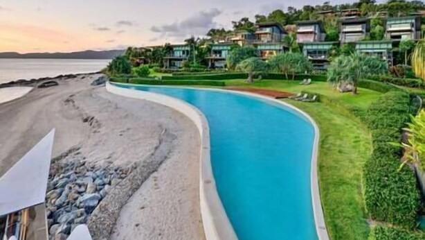 Um resort com piscina em curva, frente ao mar e vegetação exuberante.