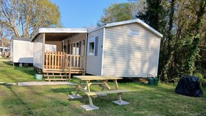 A mobile home with a porch and a picnic table in a grassy area.