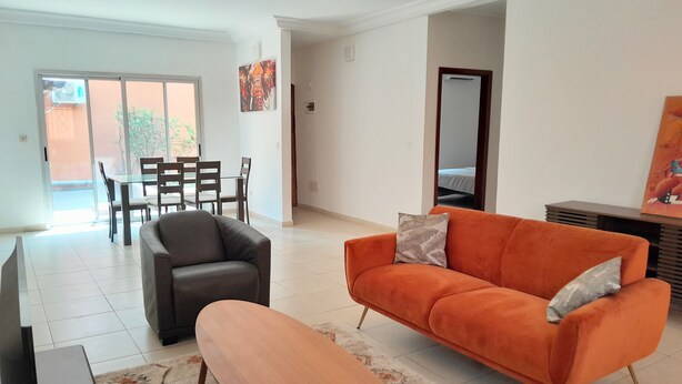 A modern living room with a sofa, a coffee table, and a TV. There is a dining area with chairs and a table. - Villa Terracotta - Abidjan - Cocody Riviera (Abidjan)