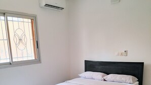 A bedroom with a bed, a window with bars, an air conditioning unit, and a wall socket. - Villa Terracotta - Abidjan - Cocody Riviera (Abidjan)