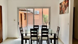 A dining area with a glass table and chairs, a sliding glass door leading to a balcony, and a painting on the wall. - Villa Terracotta - Abidjan - Cocody Riviera (Abidjan)