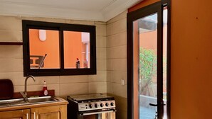 A compact kitchen with a stove, sink, and wooden cabinets. - Villa Terracotta - Abidjan - Cocody Riviera (Abidjan)