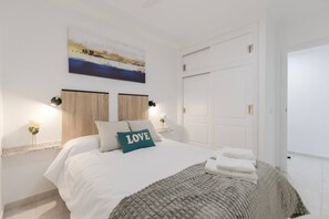 A bedroom with a bed, a painting, a door, and a nightstand with a lamp.