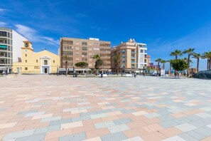 A spacious public square with a tiled floor, surrounded by multi-story buildings with commercial establishments on the ground floor. - Feel at Home by Fidalsa (La Mata)