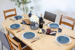 A dining table set with blue plates, silverware, a bottle of wine, a vase with flowers, and a plate of cheese and grapes. - Feel at Home by Fidalsa (La Mata)