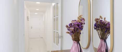 Un pasillo con una mesa de madera, dos jarrones con flores secas y dos espejos en la pared.