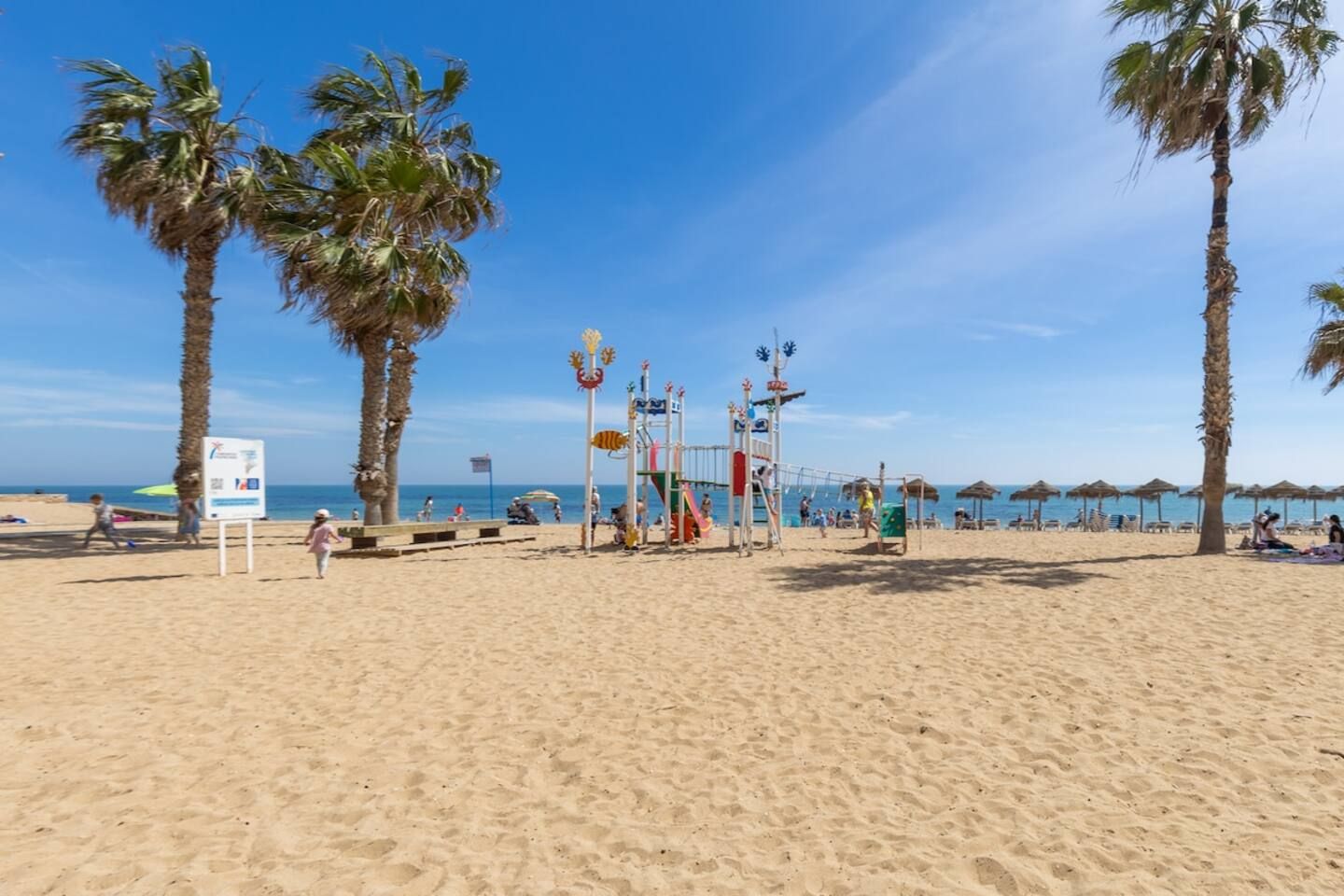 A beach with palm trees, a volleyball net, and beach umbrellas.