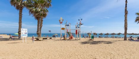 A beach with palm trees, a volleyball net, and beach umbrellas.