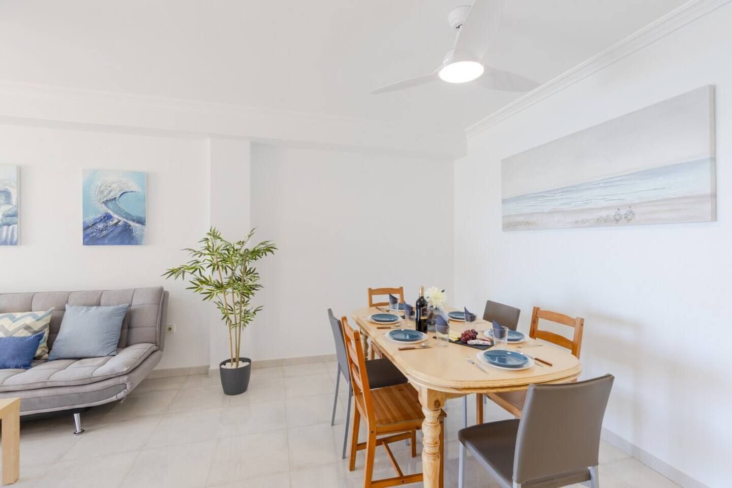 A dining area with a wooden table set for four, a grey sofa, and a bamboo plant.