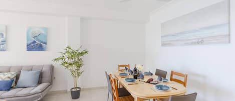 Un comedor con una mesa de madera dispuesta para cuatro personas, un sofá gris y una planta de bambú.