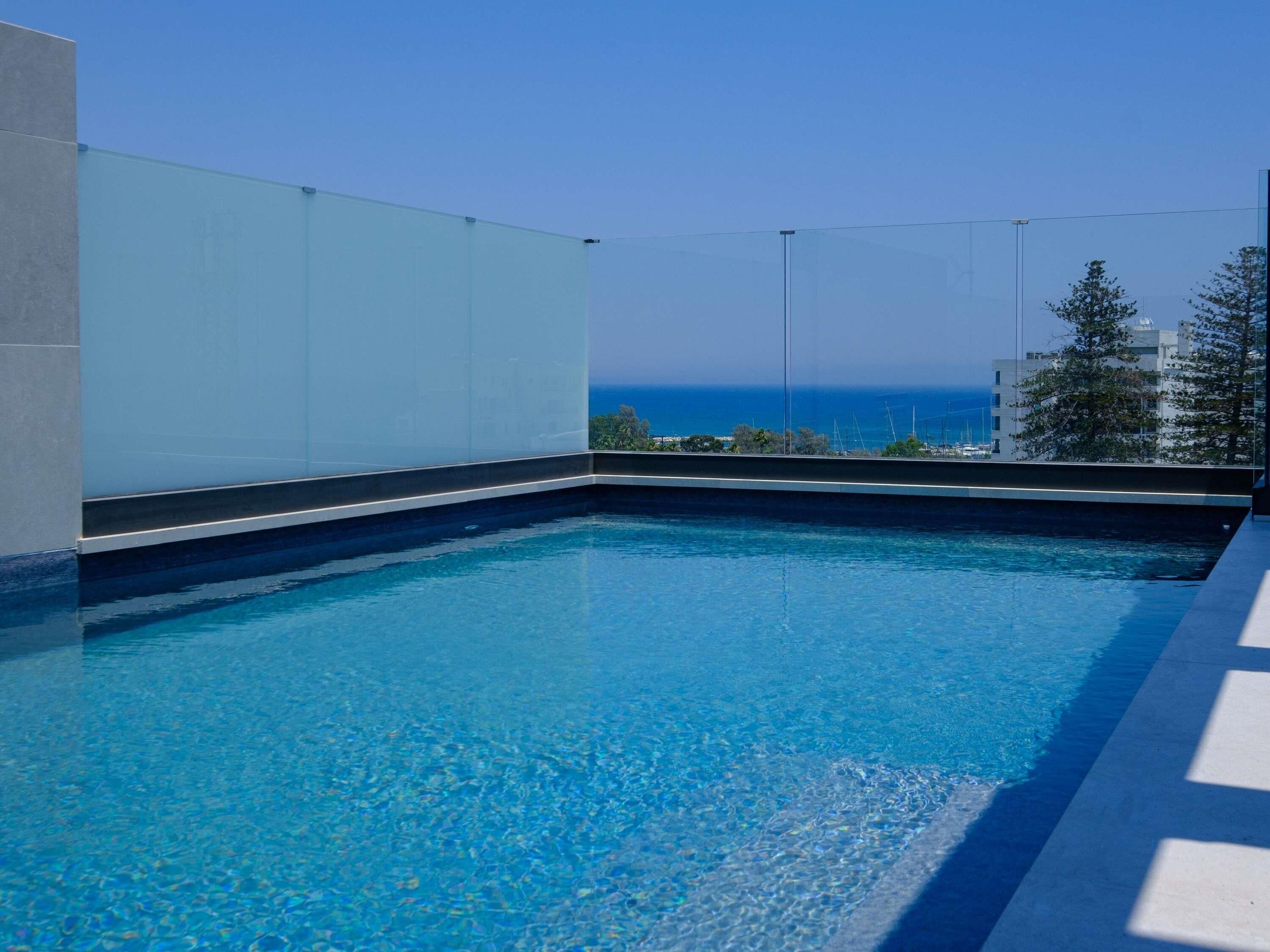 A rooftop pool with clear blue water, a view of the ocean, and a modern architectural design.