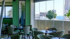 A restaurant with green walls and large windows offering a view of the city and the sea. - Mercure Larnaca Finikoudes Beach (Larnaca)