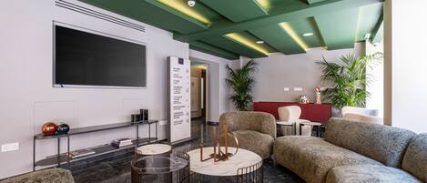 A modern lobby with a sectional sofa, a round coffee table, and a flat-screen TV mounted on the wall.