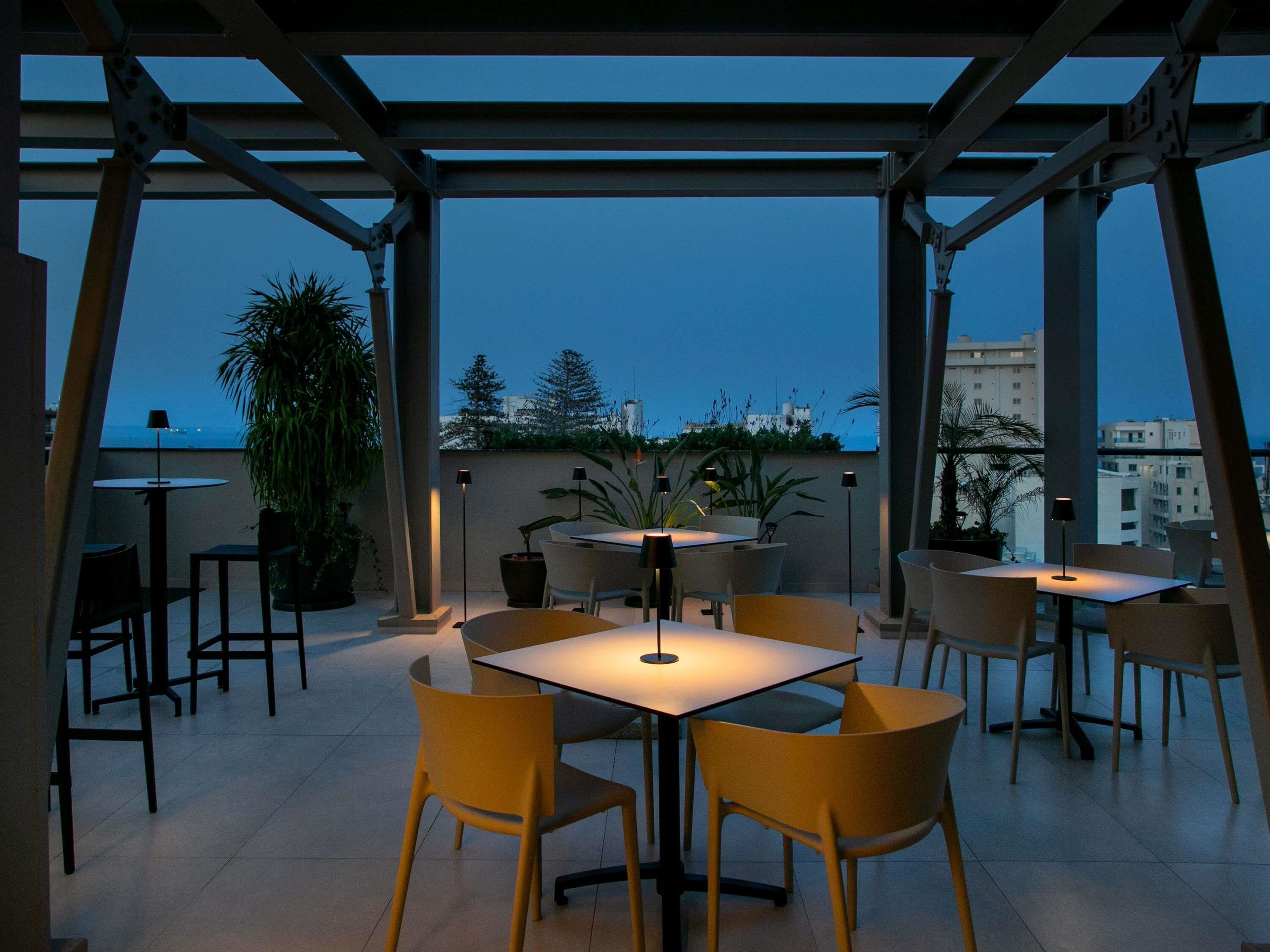 An outdoor patio area with tables and chairs, surrounded by a metal pergola structure.